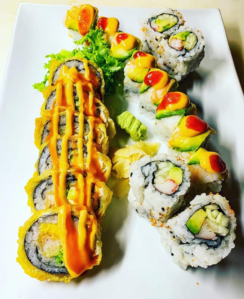 A white plate holds three types of sushi rolls, including tempura, California, and avocado-topped.